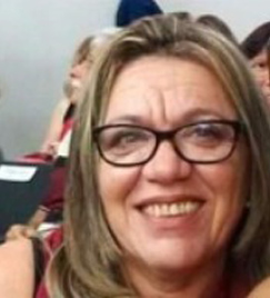 Foto de uma mulher de óculos em seus 50 anos retratada do ombro para cima. Ela tem cabelo loiro liso, usado na altura do queixo. O rosto da mulher ocupa a maior parte da imagem.