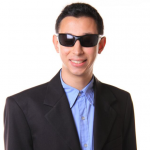 Foto de Daniel Marllon, um homem branco de cerca de 30 anos, com deficiência visual. Ele sorri na foto, usando óculos escuros, terno preto e camisa azul.