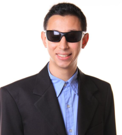 Foto de Daniel Marllon, um homem branco de cerca de 30 anos, com deficiência visual. Ele sorri na foto, usando óculos escuros, terno preto e camisa azul.